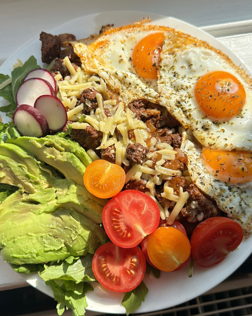 A balanced plate of eggs, avocado, greens and tomato